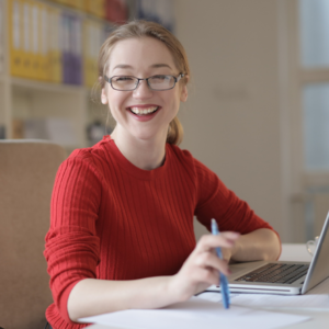 woman with glasses smiling while studying for LSAT on laptop