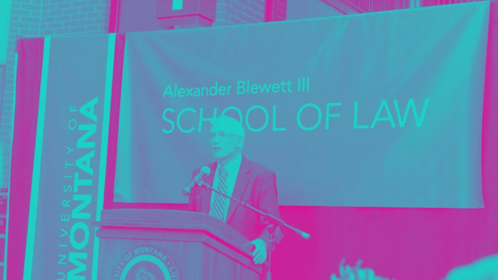 A man speaking on the podium with a banner of the Alexander Blewett III School of Law in the background.